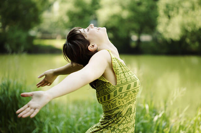 Ženska v zeleni obleki na travi, roke ima nazaj, osločen hrbet, uživa v naravi