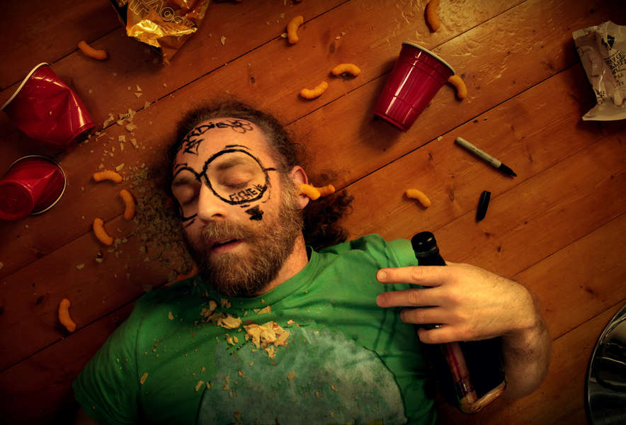 Moški leži na tleh, in spi po naporni zabavi, okoli njega smeti, na obrazu ima s flomastrom narisane očala